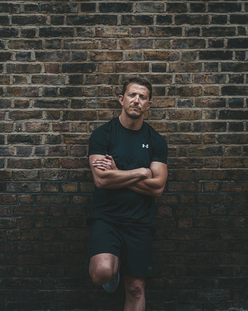 Tom, personal trainer bij SculptClub, tegen een bakstenen muur